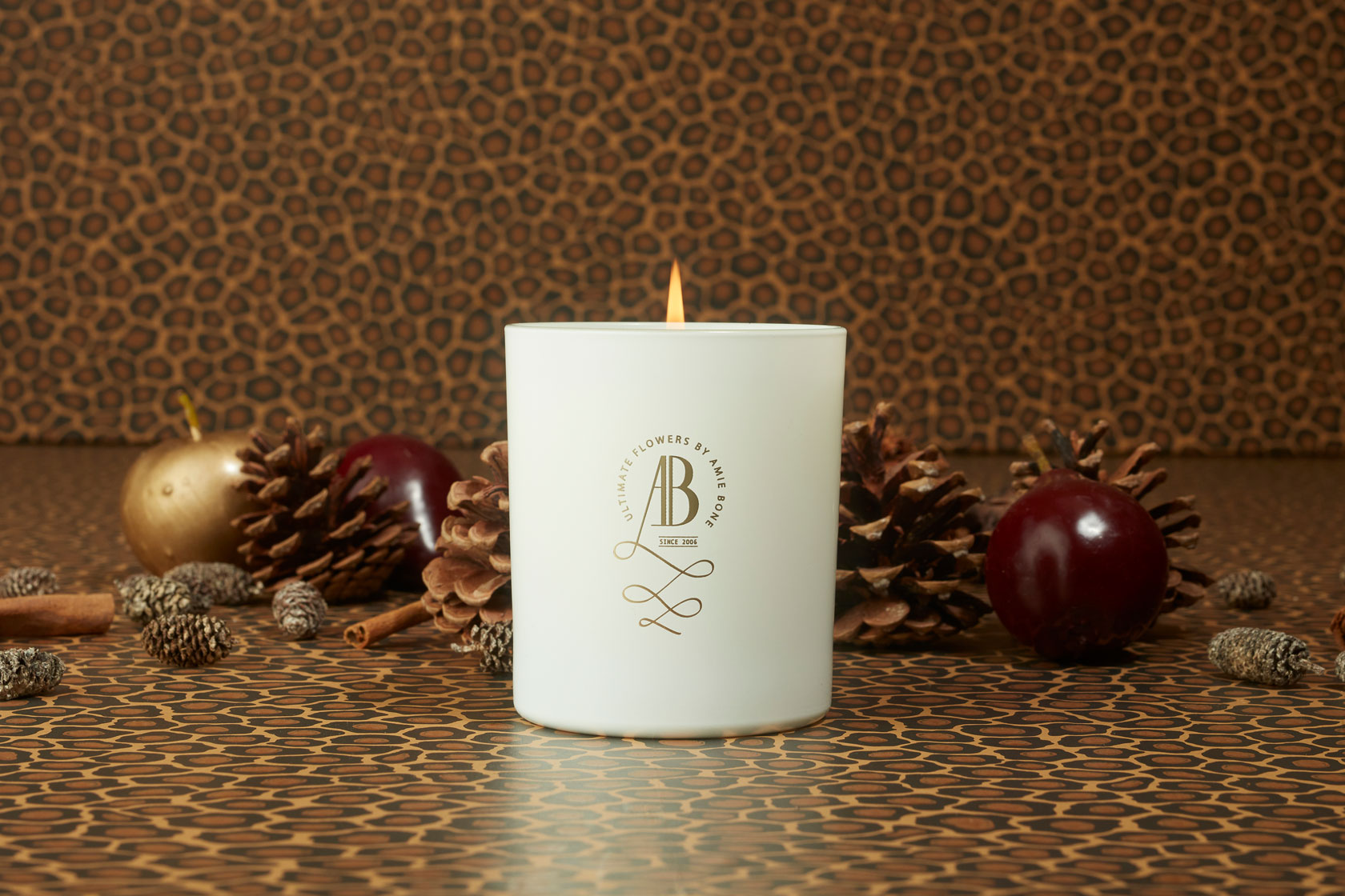 a white candle with an iconic gold crested logo sitting next to a white gift box tied in black ribbon