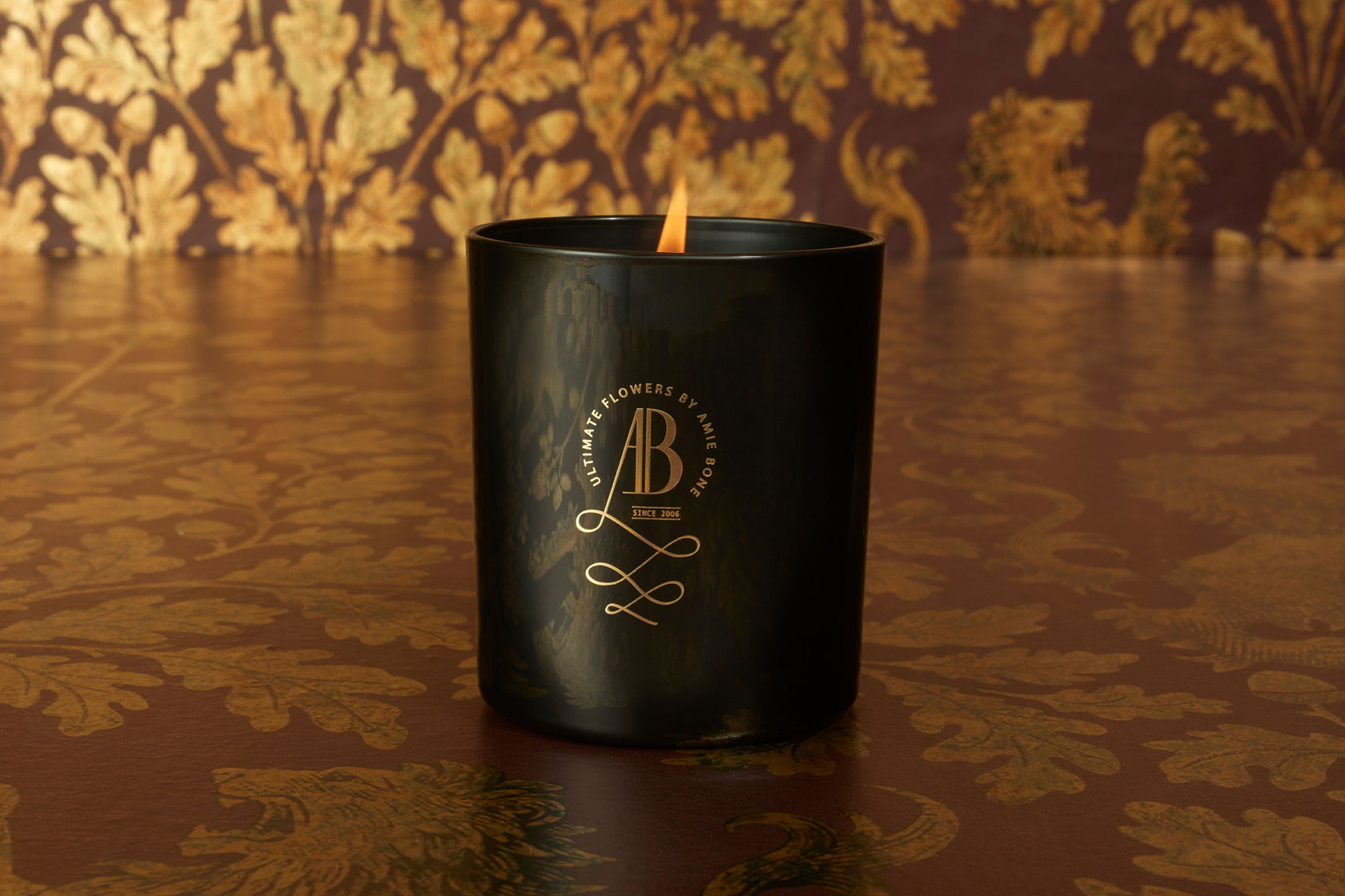 a black candle with an iconic gold crested logo sitting next to a black gift box tied in black ribbon