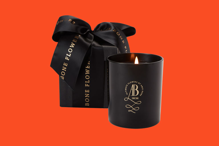 a black candle with an iconic gold crested logo sitting next to a black gift box tied in black ribbon
