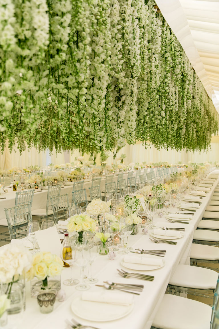 a long dining table inside a marquee with delphiniums suspended above