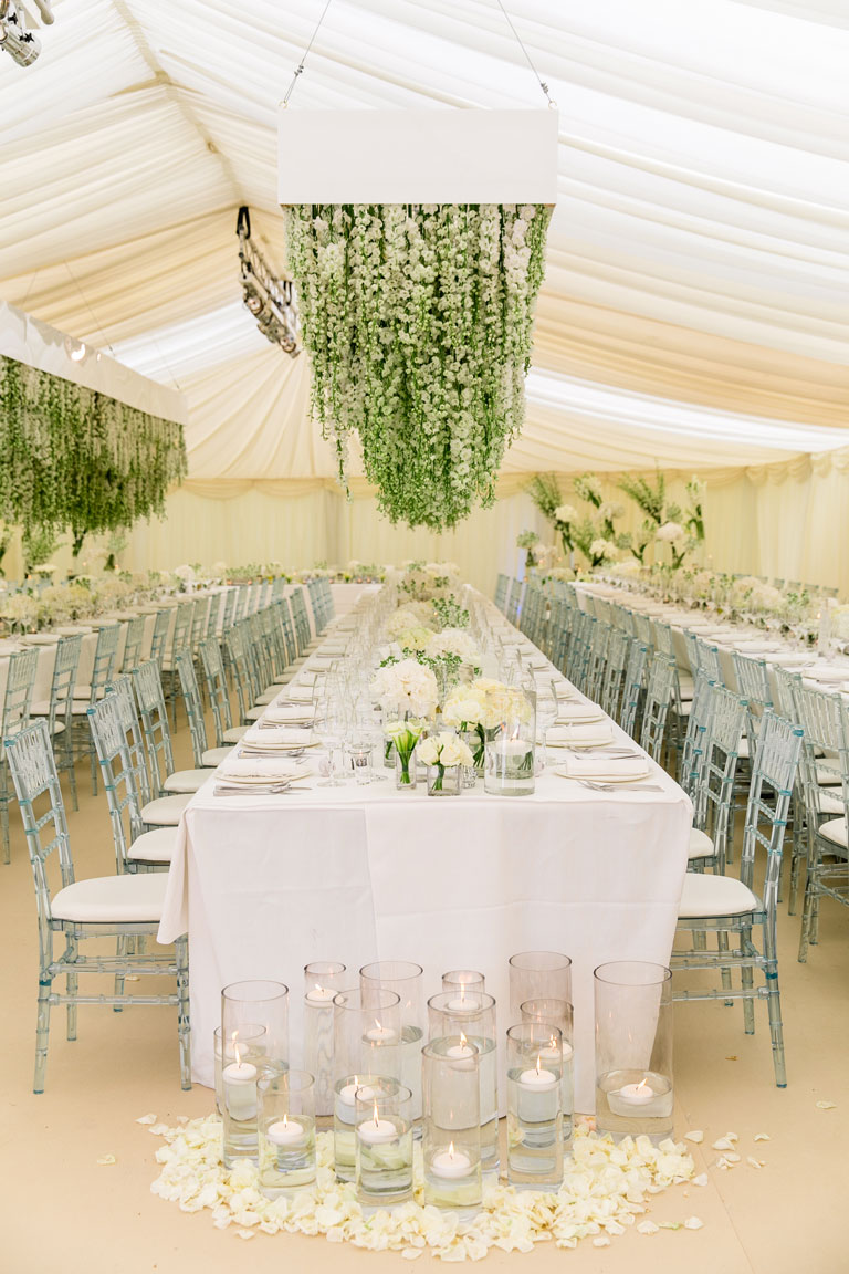 long table at a wedding with suspended white flowers hanging from the ceiling of a marquee
