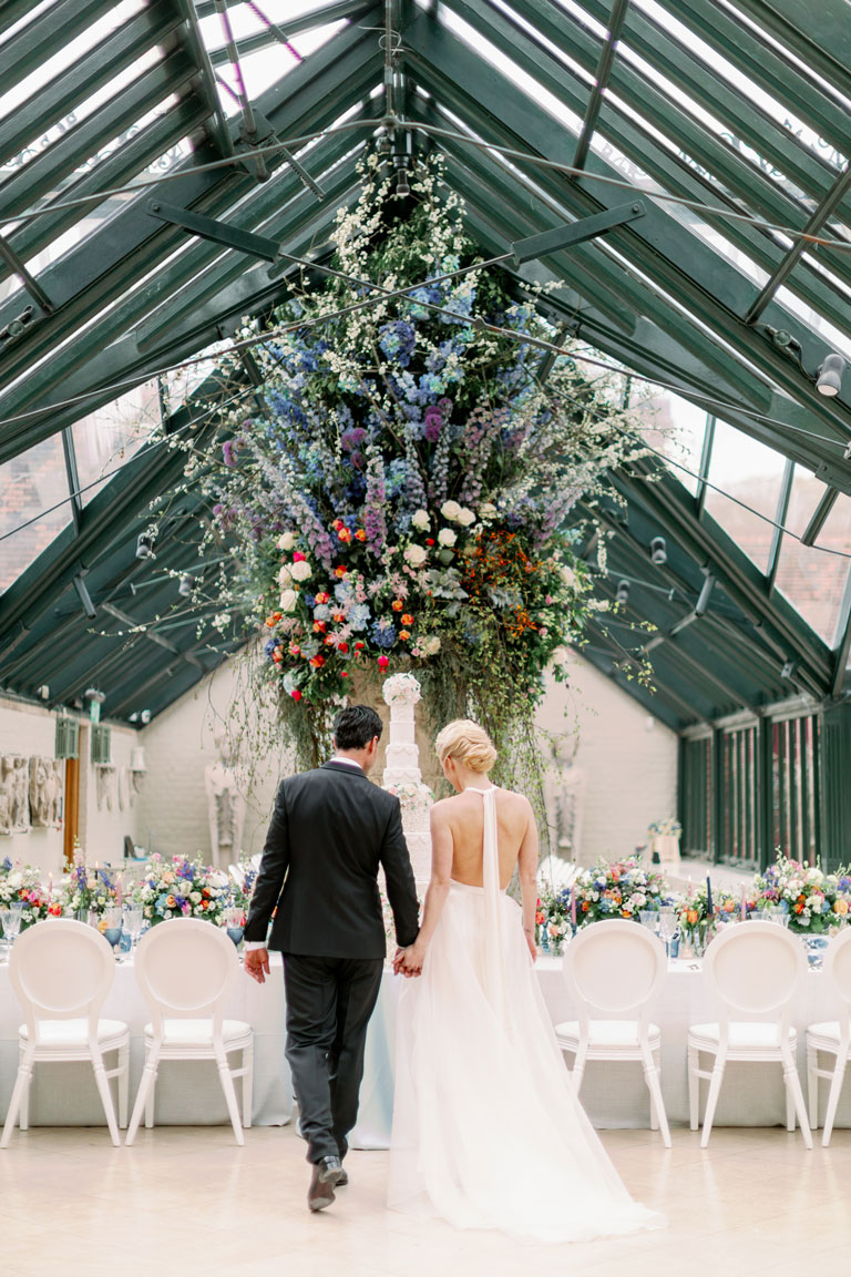 a giant urn bursting with flowers in an orangery for a wedding with the bride and groom
