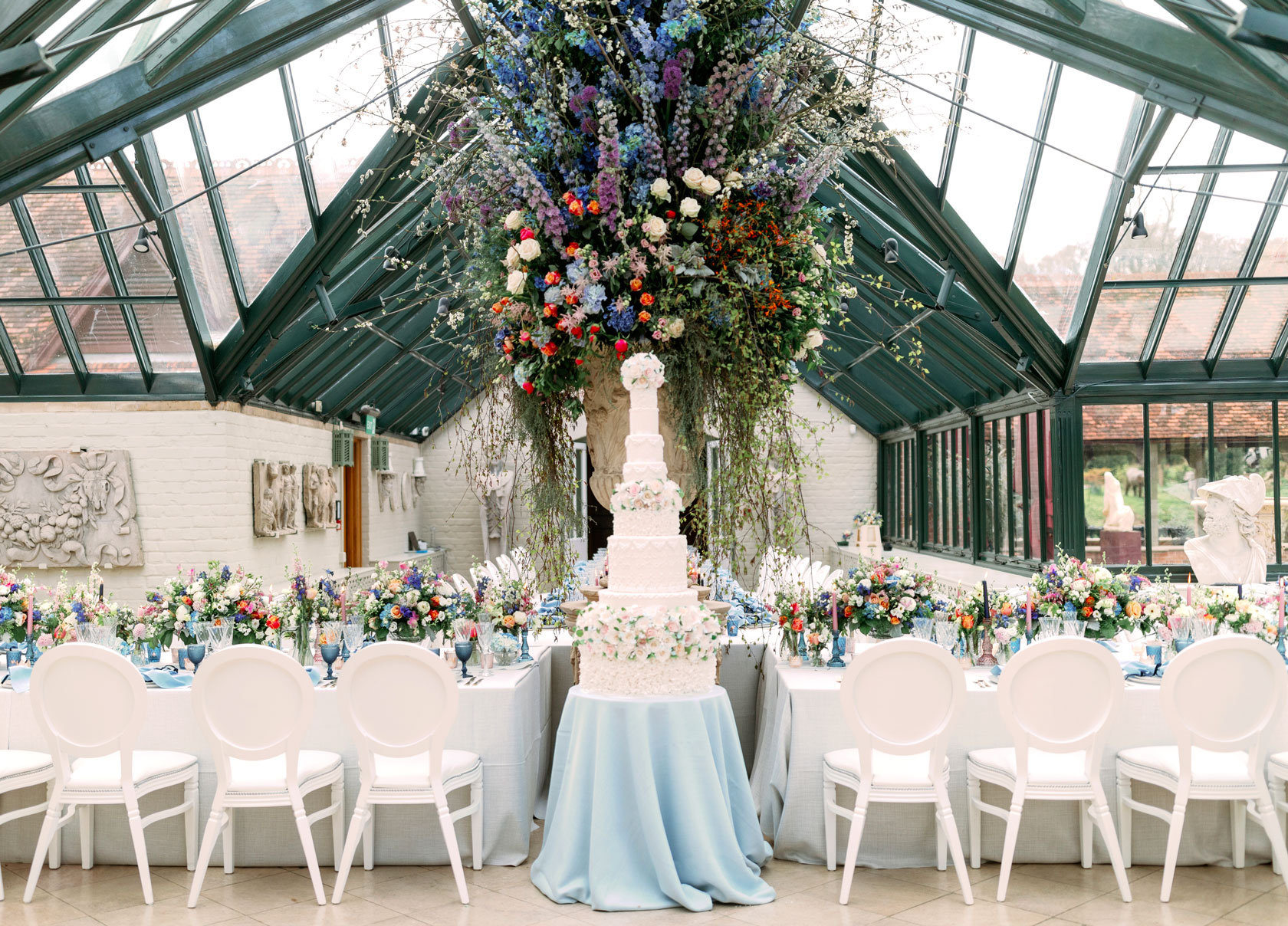 a huge wedding cake in an orangery surrounded by beautiful flowers and floral tablescape