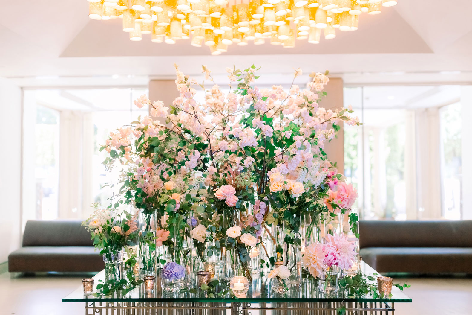 entrance table in a hotel with loads of flowers in vases in a colour palette of blush pink, lilac, cream and poweder blue surrounded by candles